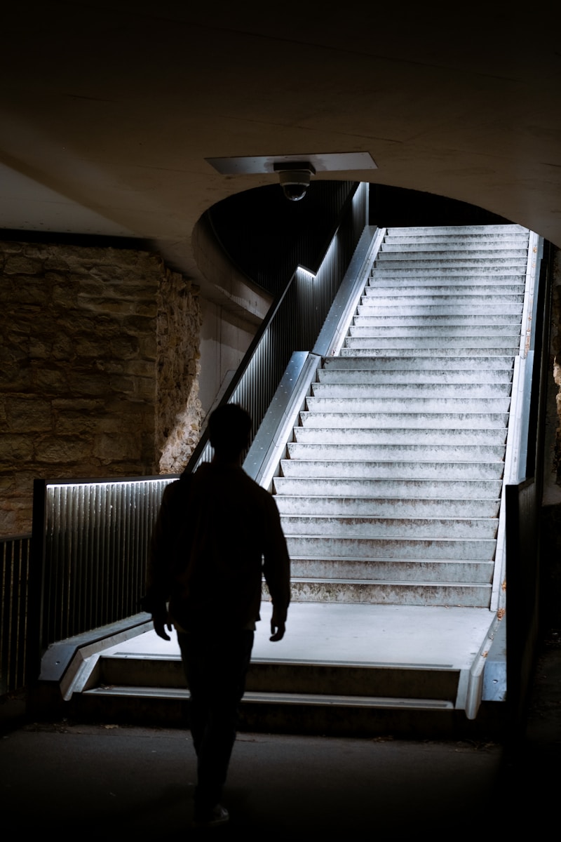 A person climbs a set of wooden steps up to a porch, viewed from below in morning light.