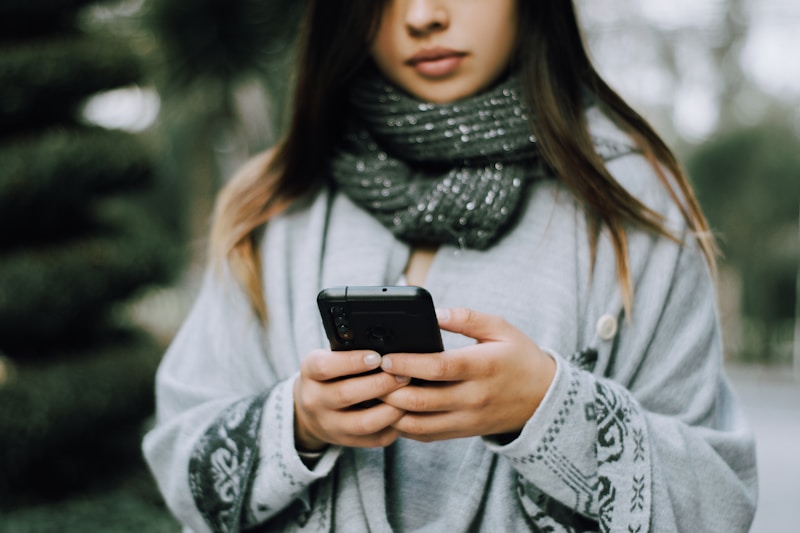 A person checks a phone while standing at a city bus stop in daytime.