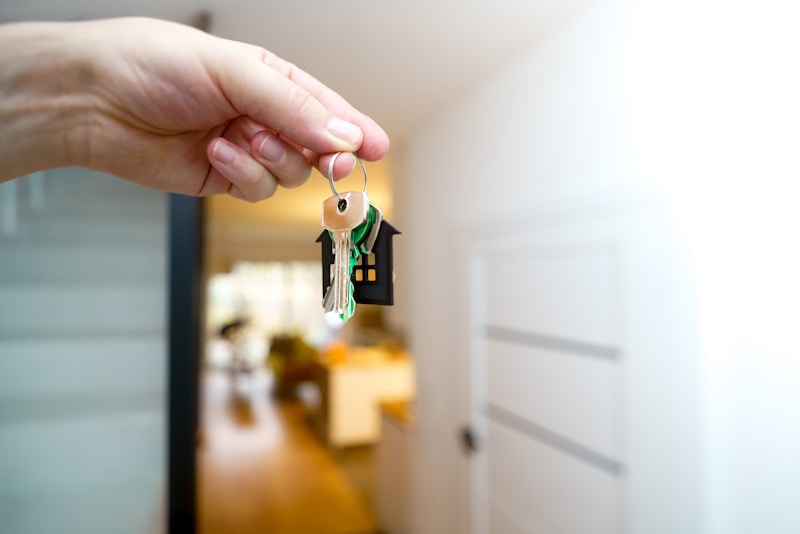 A hand turns a key in the front door of an apartment, with afternoon light falling across the threshold.